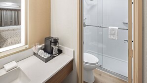A modern bathroom with a glass-enclosed shower, a white toilet, and a countertop with a coffee maker and toiletries.