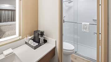 Un bany modern amb dutxa de vidre, un vàter blanc i una superfície amb una cafetera i productes de tocador.