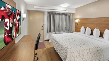 Una habitación de hotel con una cama grande, un escritorio, una silla, un televisor y una ventana con cortinas.