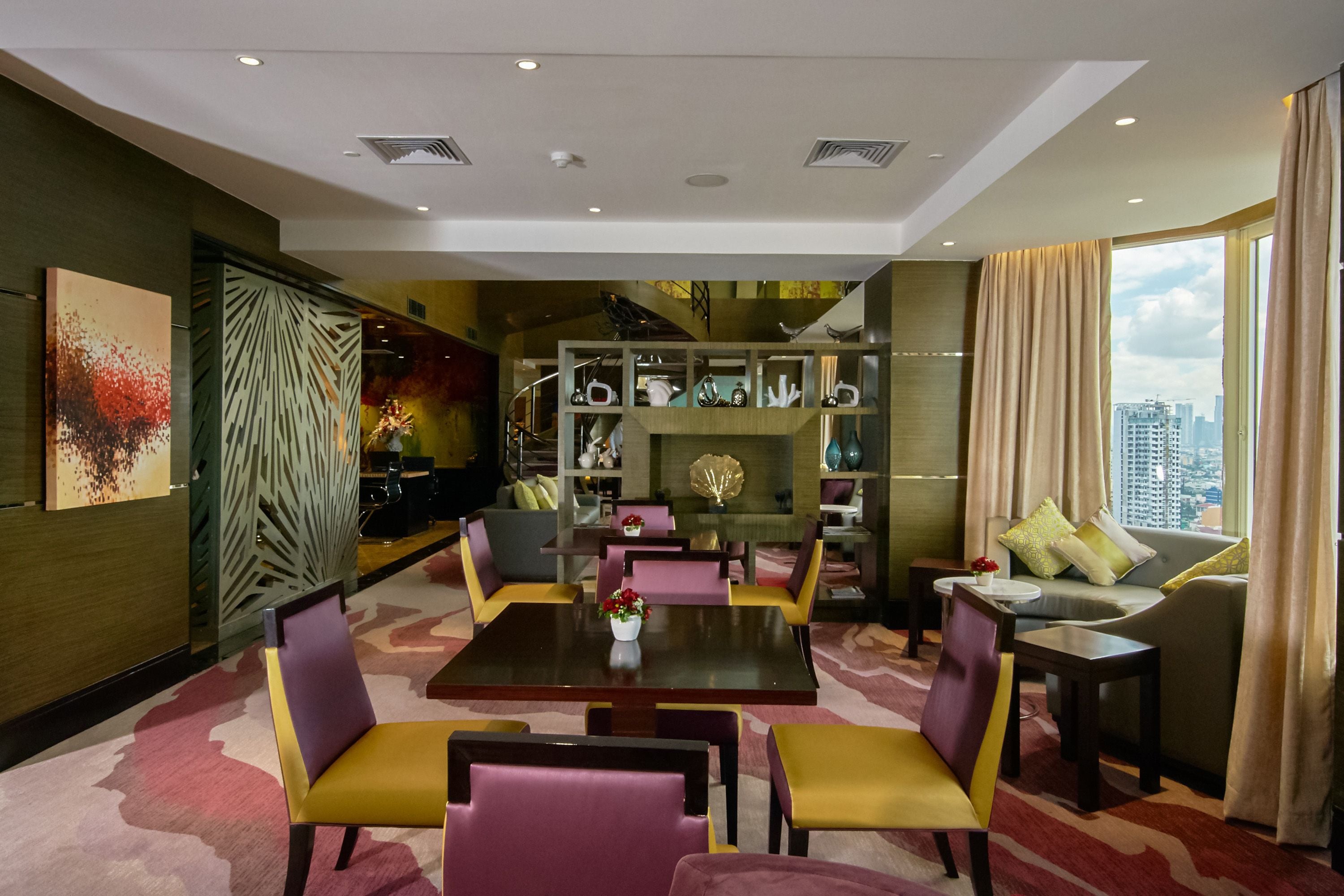 A modern hotel lobby with a central dining area, seating arrangements, and a view of the cityscape.