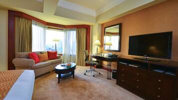 Une chambre d’hôtel avec un lit, un canapé, un bureau, une télévision et une fenêtre avec des rideaux.