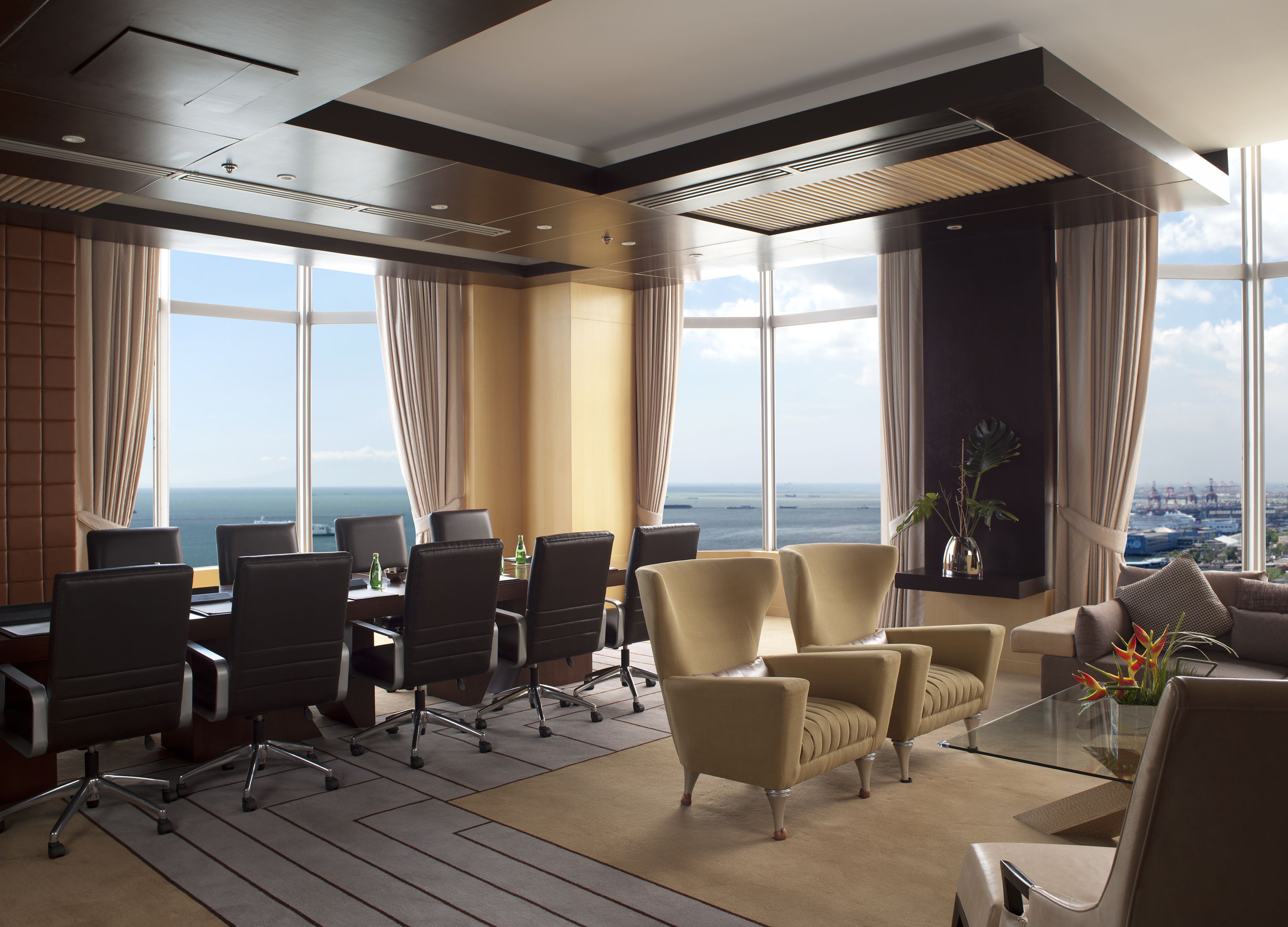 Une salle de conférence moderne offrant une vue panoramique sur l’océan, avec une table en verre, des fauteuils en cuir et une grande fenêtre.