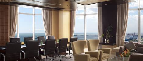 Een moderne vergaderruimte met panoramisch uitzicht op zee, voorzien van een glazen tafel, lederen stoelen en een groot raam.