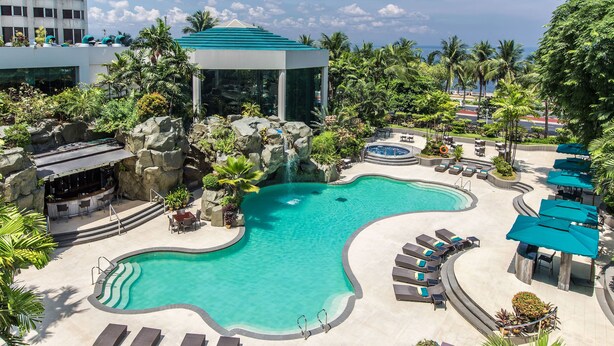 A resort pool area with a clear blue pool, lounge chairs, and a waterfall feature. - Diamond Hotel Philippines (Manila)