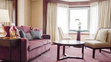 Habitación de hotel con sofá, sillón, mesa redonda, lámpara y vistas al exterior a través de una ventana.