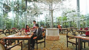 Un restaurante con varias mesas y sillas, ventanas amplias y un árbol decorativo en el centro.
