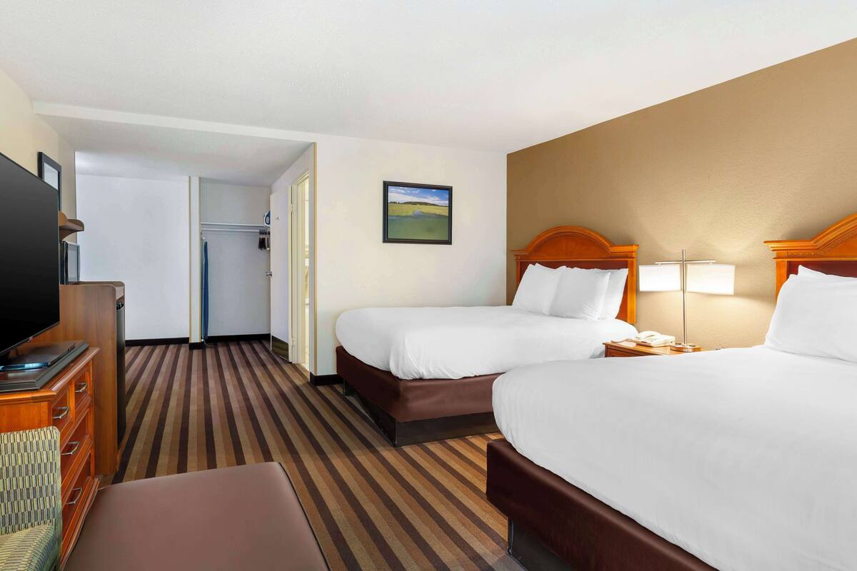 A hotel room with two beds, a TV, a desk, and a painting on the wall.