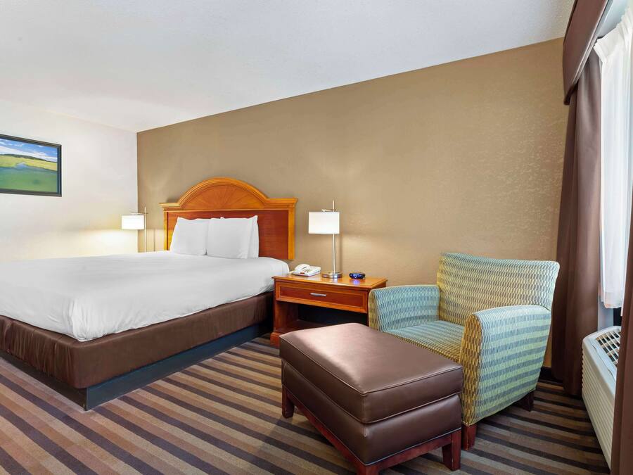 Une chambre d’hôtel avec un grand lit, une table de chevet avec une lampe, une chaise et un pouf.