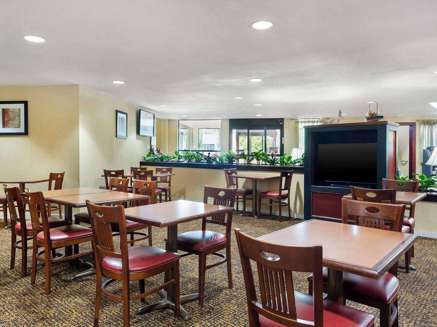 Un comedor de hotel con varias mesas y sillas de madera, un televisor y una pequeña decoración de barco en la pared.