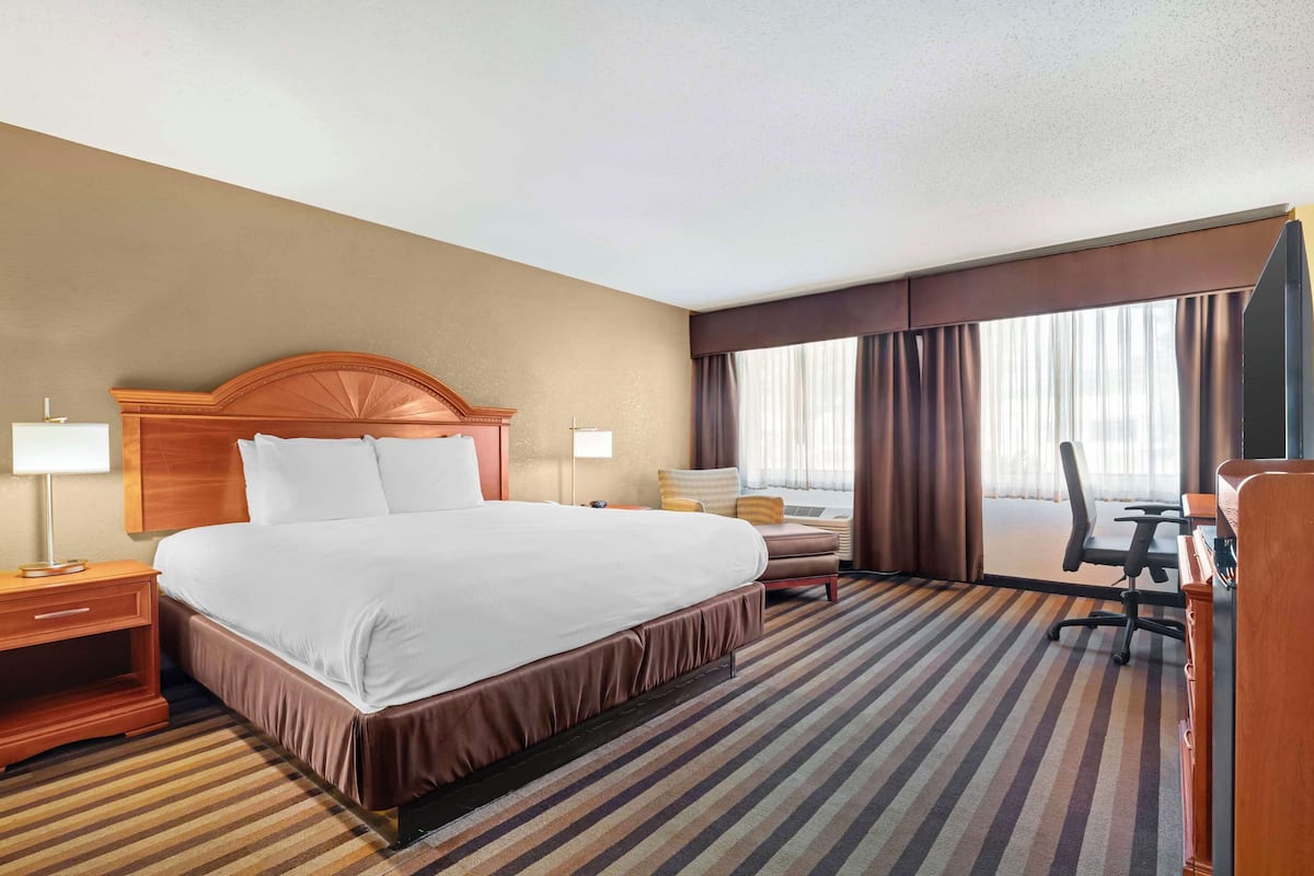 A hotel room with a large bed, a desk, a chair, and a TV.