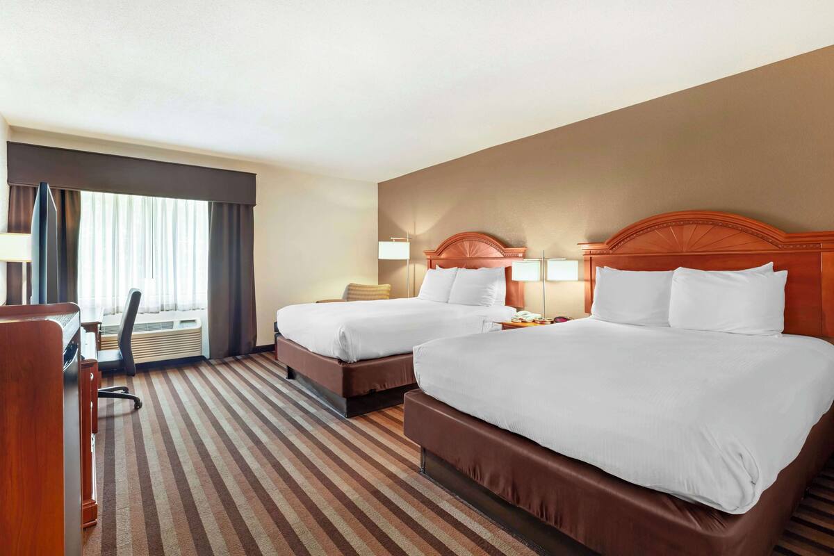 A hotel room with two beds, a desk, and a chair.