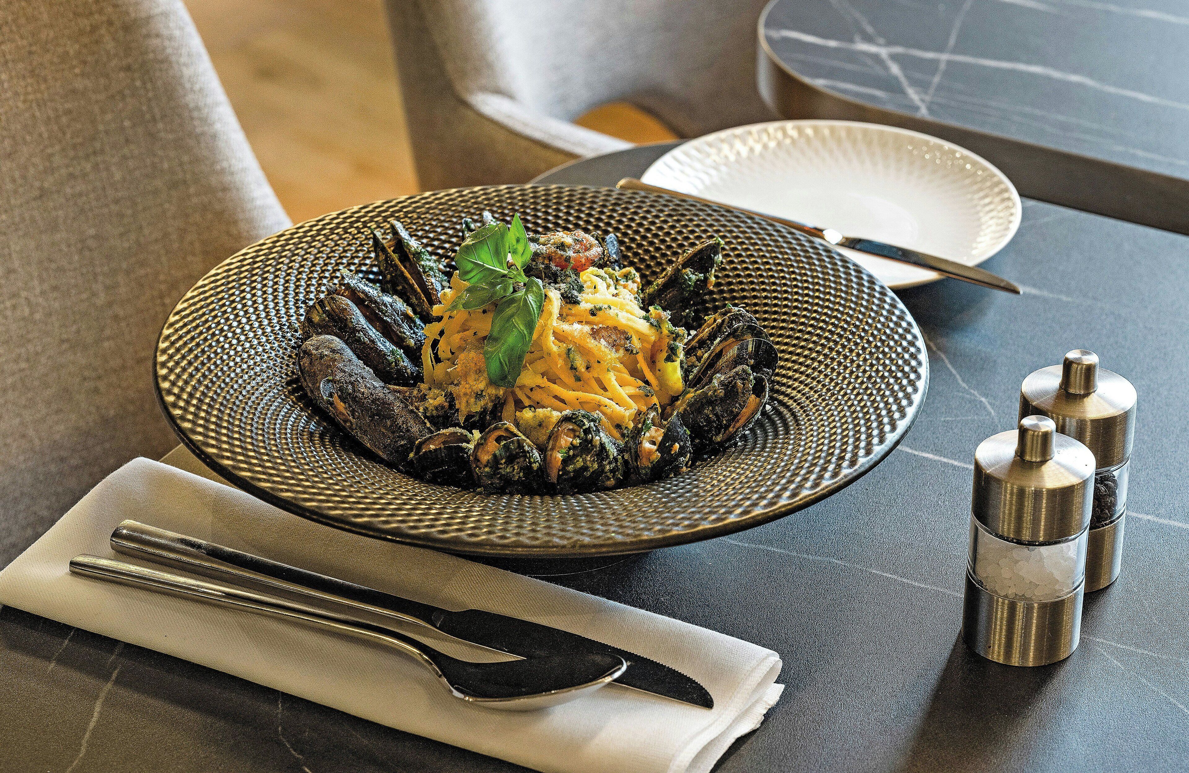 A plate of mussels with a garnish, a knife, and a spoon on a table.
