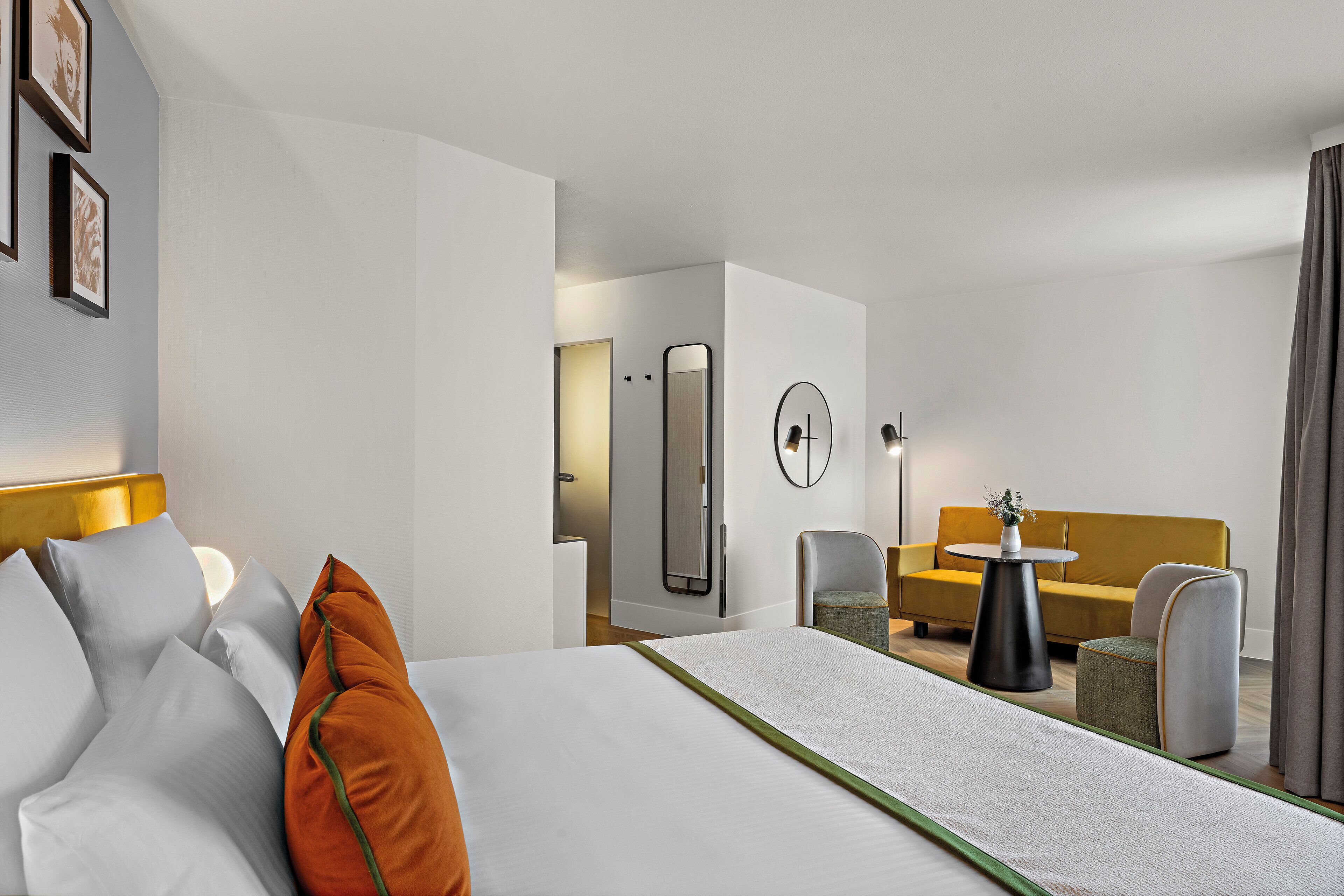 A hotel room with a bed, a sofa, a chair, a small table, and a mirror.