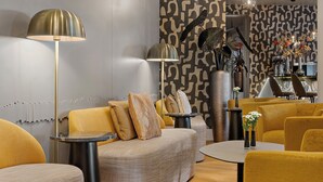 A modern living room with a sofa, yellow chairs, a round table, and a floor lamp. - Leonardo Hotel Mainz (Mainz)