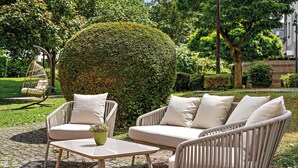 An outdoor seating area with wicker furniture and a round table, surrounded by well-maintained hedges and trees. - Leonardo Hotel Mainz (Mainz)