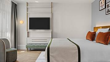 A modern hotel room with a large bed, a flat-screen TV, a seating area with a chair, and a small table.
