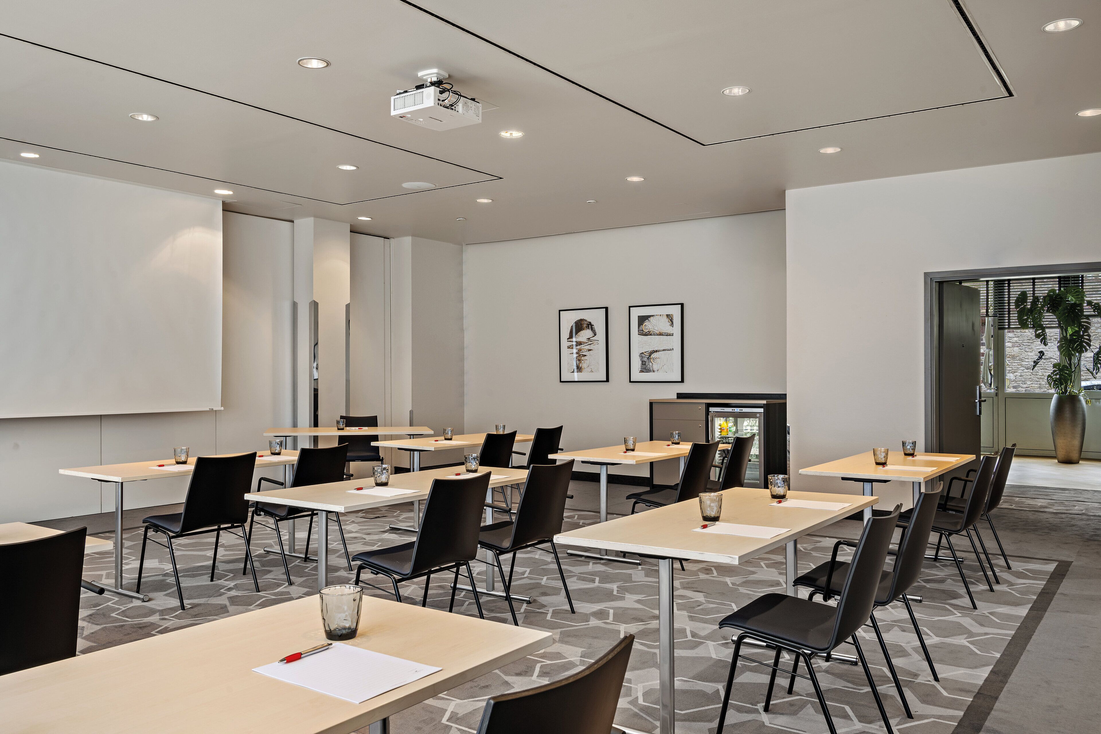 A modern conference room with multiple tables and chairs, a projector, and framed artwork on the walls.