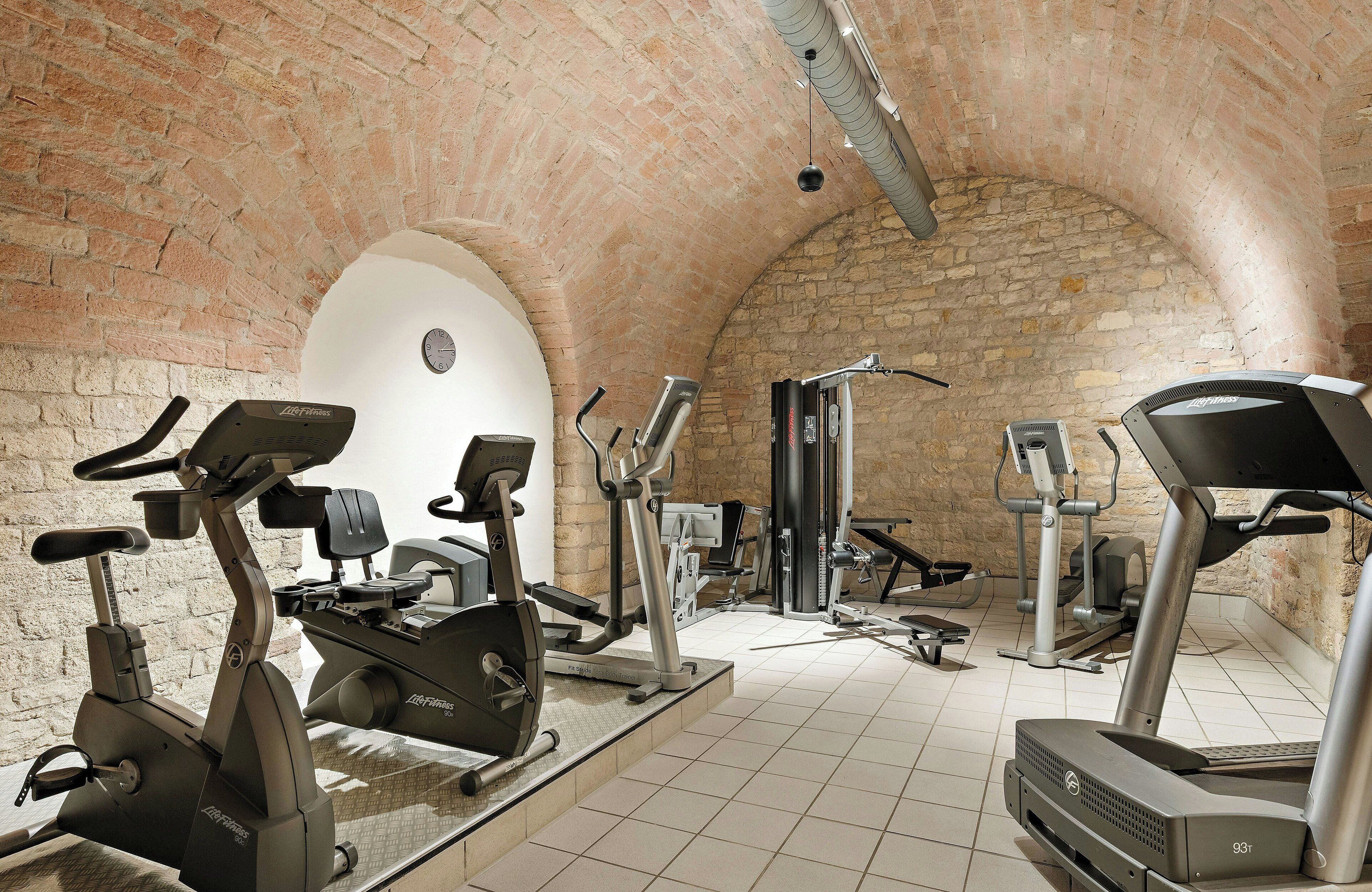 A gym with various exercise machines, a brick wall, and a tiled floor.
