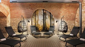 A spa area with black lounge chairs, a mural of a forest, and stone walls. - Leonardo Hotel Mainz (Mainz)