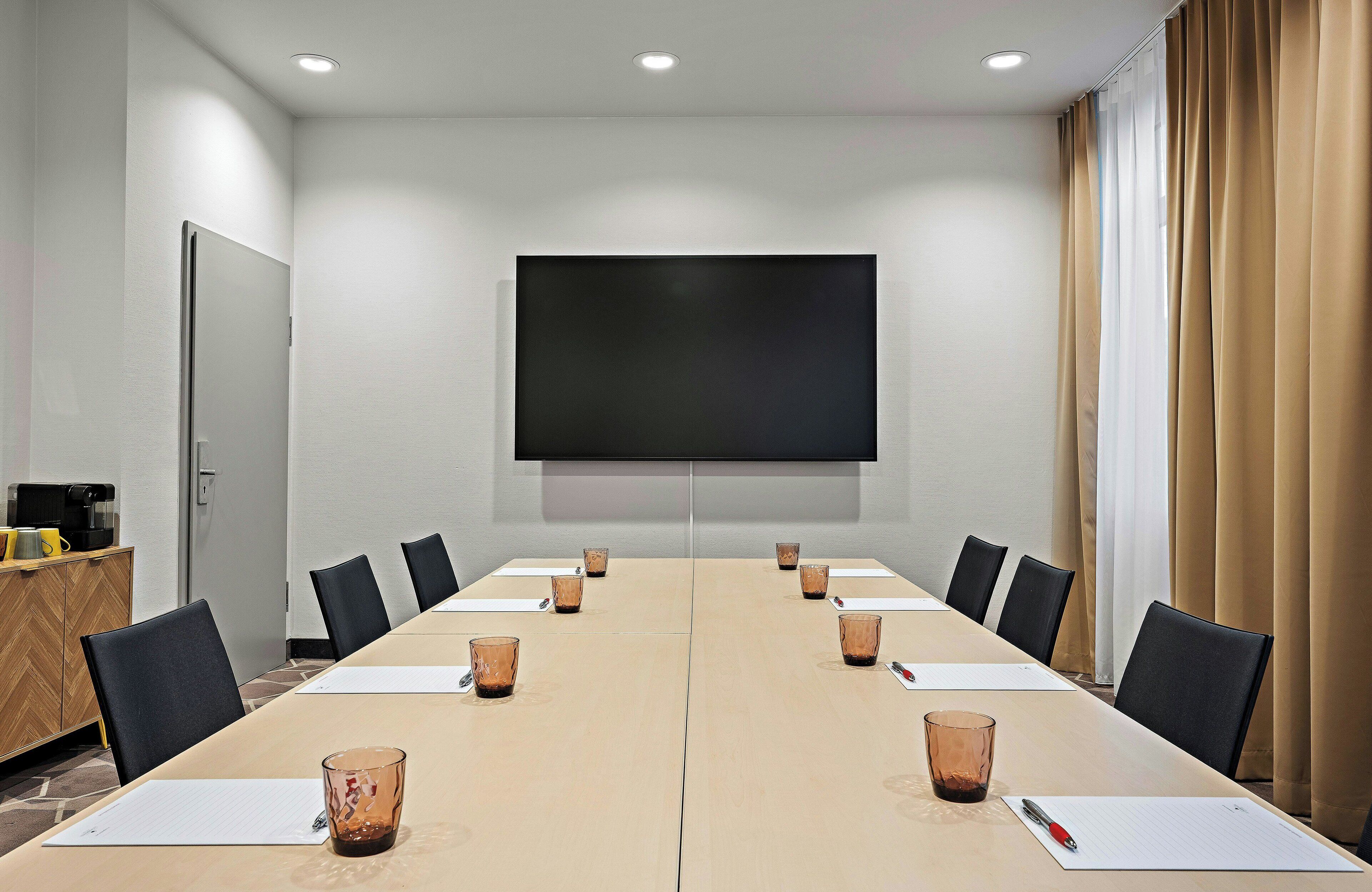 A conference room with a long table, chairs, a projector screen, and a coffee machine.