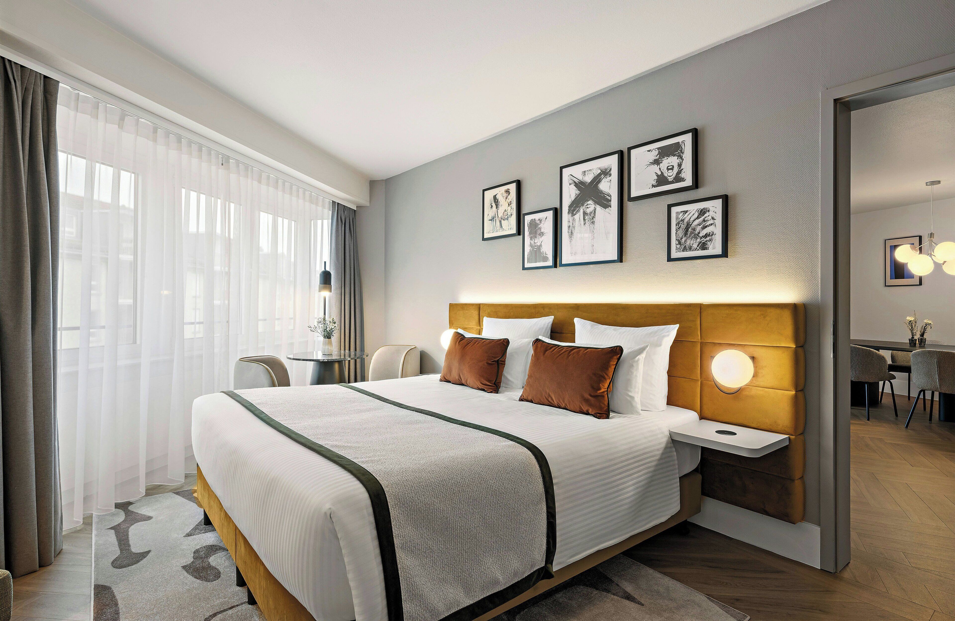 A modern hotel room with a large bed, bedside tables, a desk, and a dining area.
