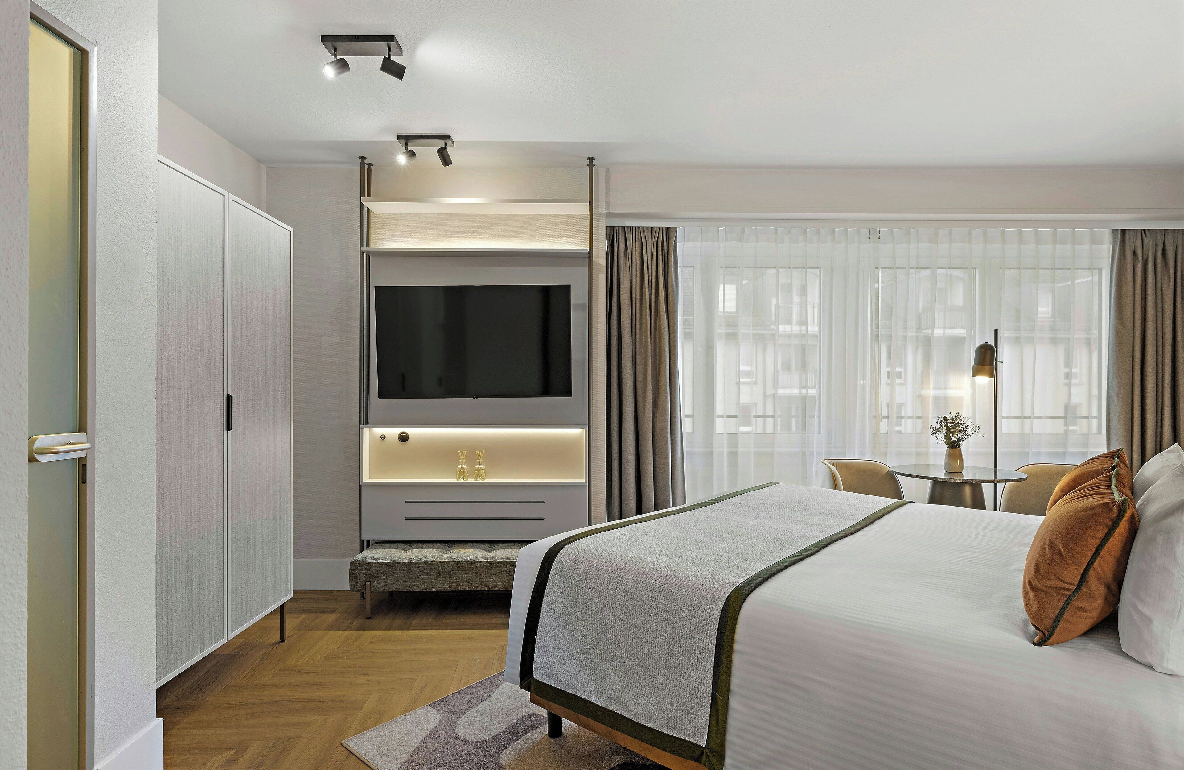 Una habitación de hotel moderna con una cama, un televisor, un escritorio y una ventana con cortinas.