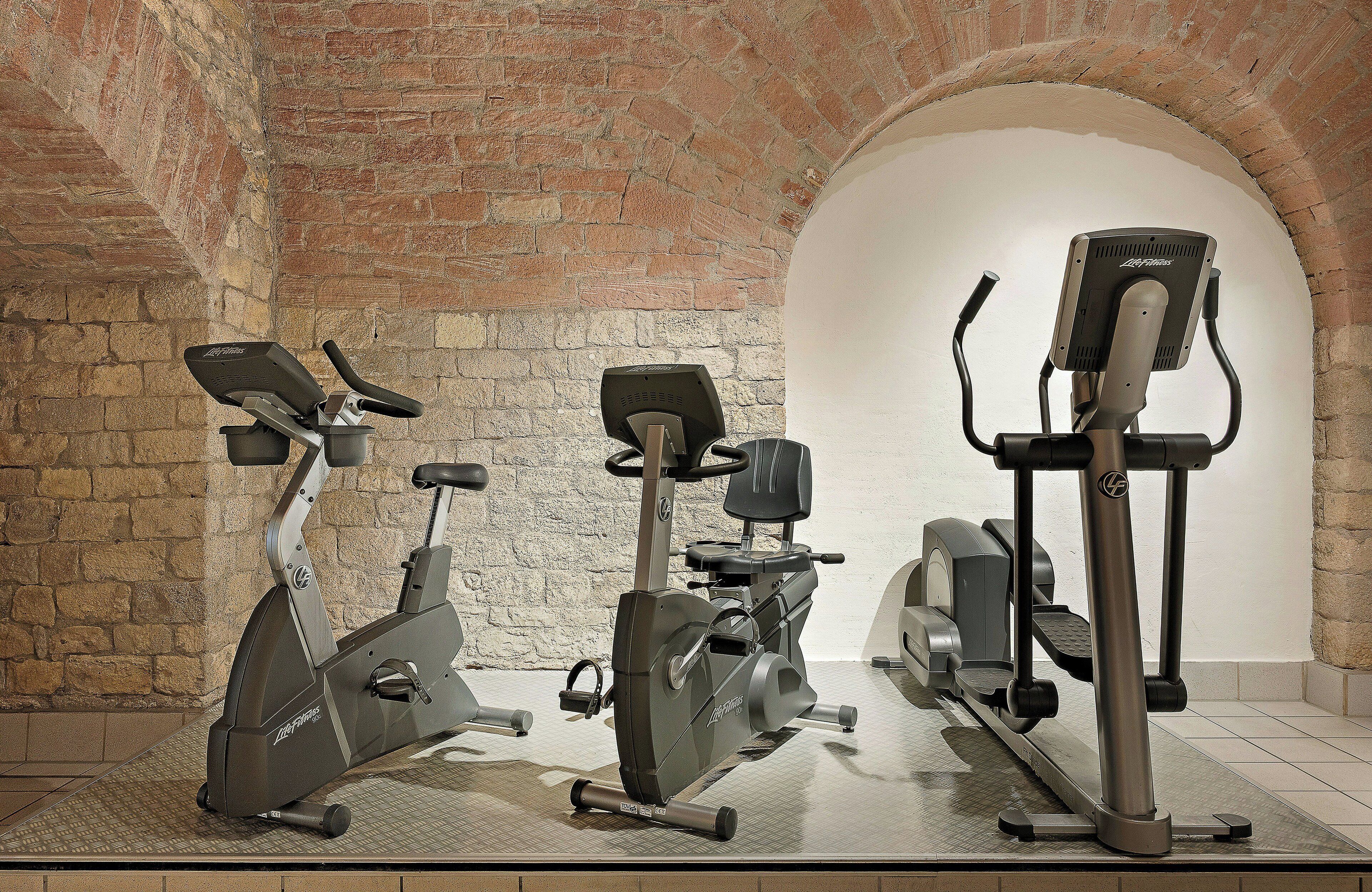 Three stationary bikes in a room with brick walls and an arched ceiling.