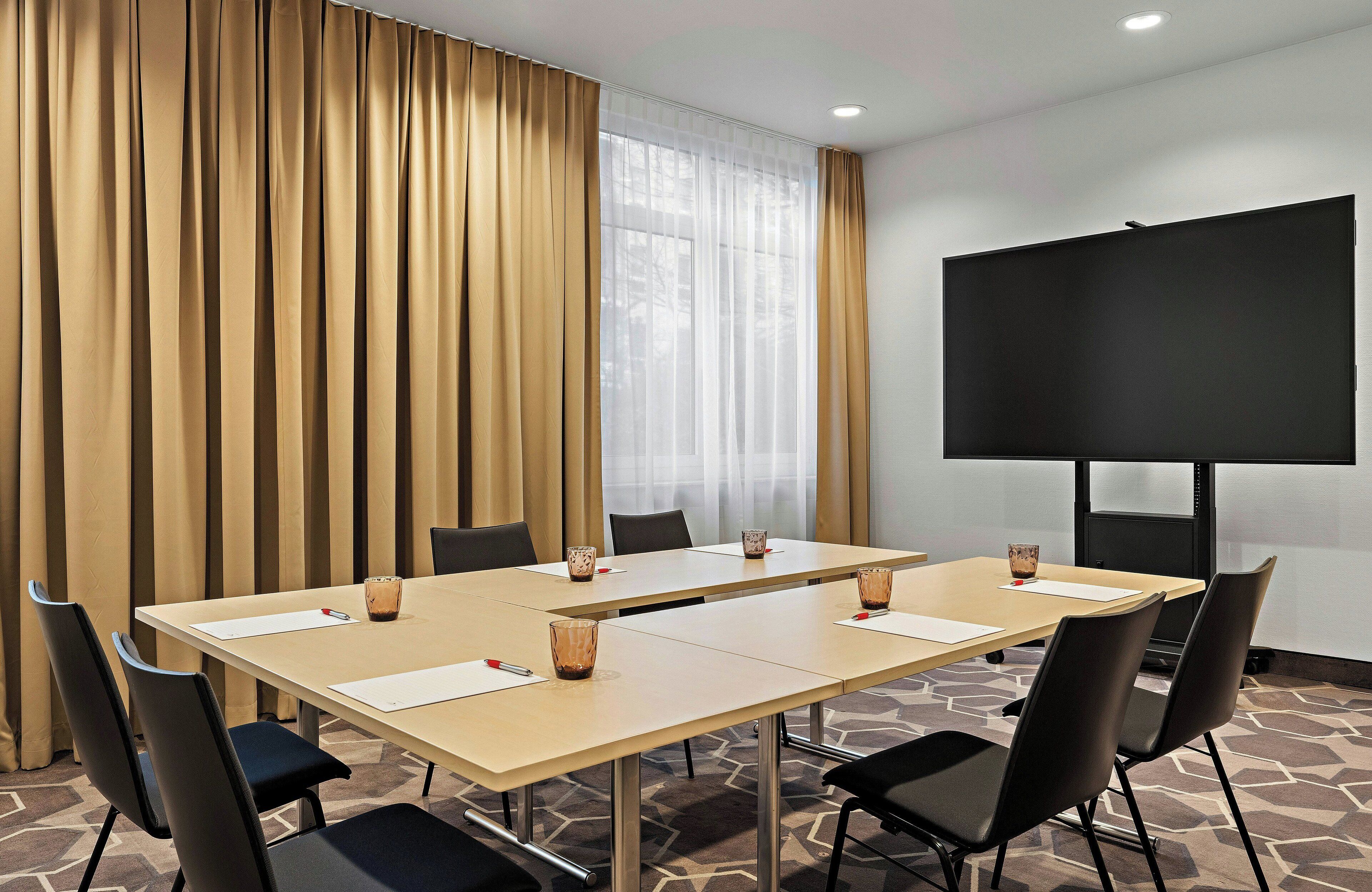 A conference room with a long table, chairs, a projector screen, and a large window with curtains.