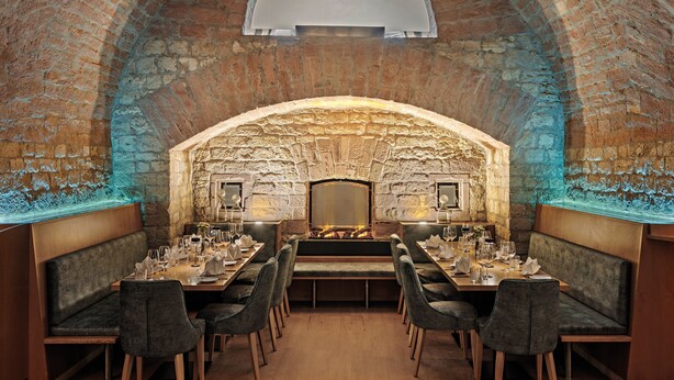 A restaurant with a brick interior, wooden tables, and cushioned seating. - Leonardo Hotel Mainz (Mainz)