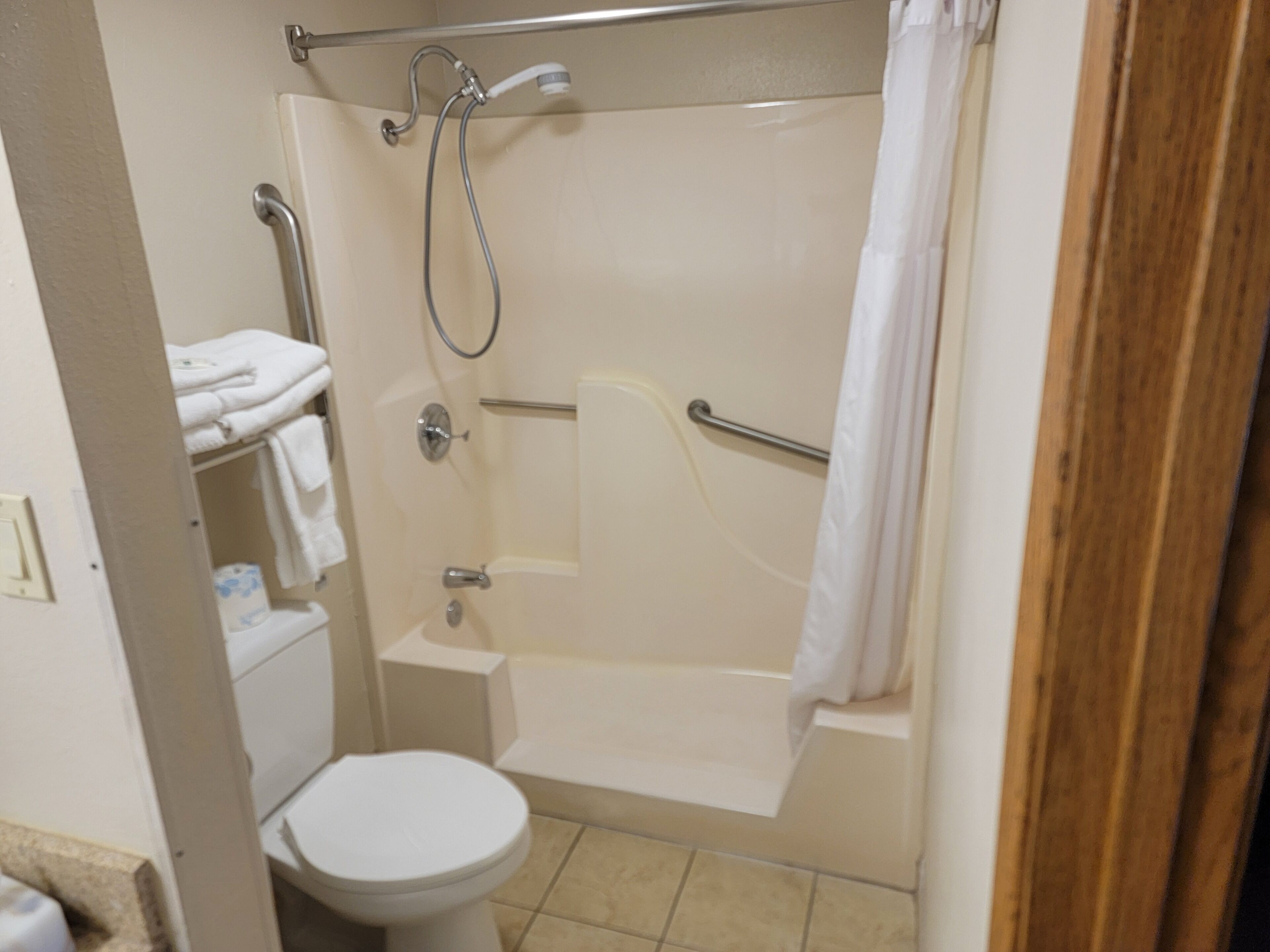 Un baño con inodoro, ducha con barra de apoyo y bañera.