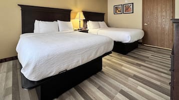 A hotel room with two beds, a nightstand with a lamp, a wooden door, and a framed picture on the wall.