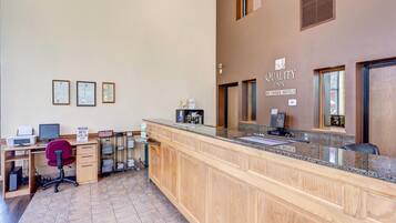 A hotel reception area with a wooden reception desk, a computer, a printer, and a sign for 'The Dish'.