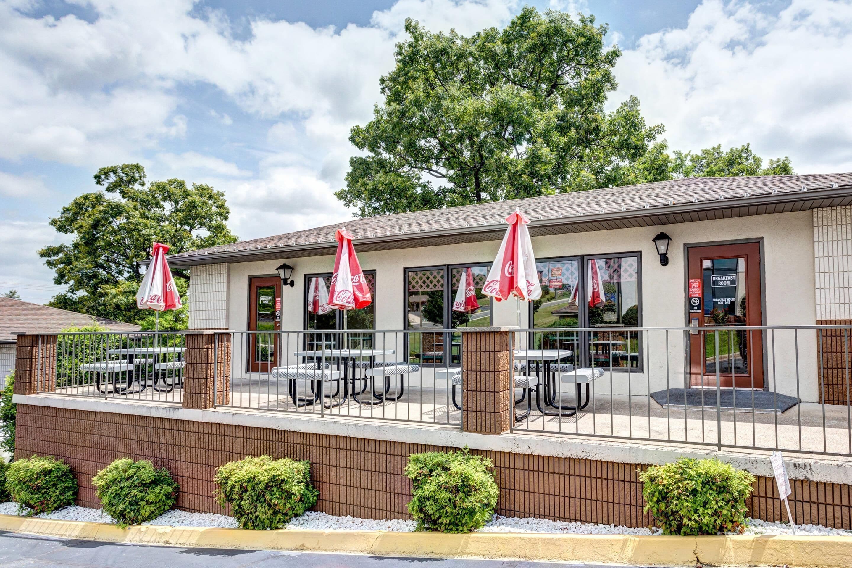 A restaurant with outdoor seating, a Coca-Cola branded awning, and a sign indicating breakfast hours.