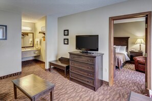 A hotel room with a bed, a television, a dresser, a desk, and a bathroom with a sink and mirror.