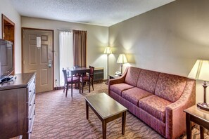 A hotel room with a sofa, a coffee table, a TV, a desk, and a chair. - Quality Inn West-Branson Theatre District (Branson)