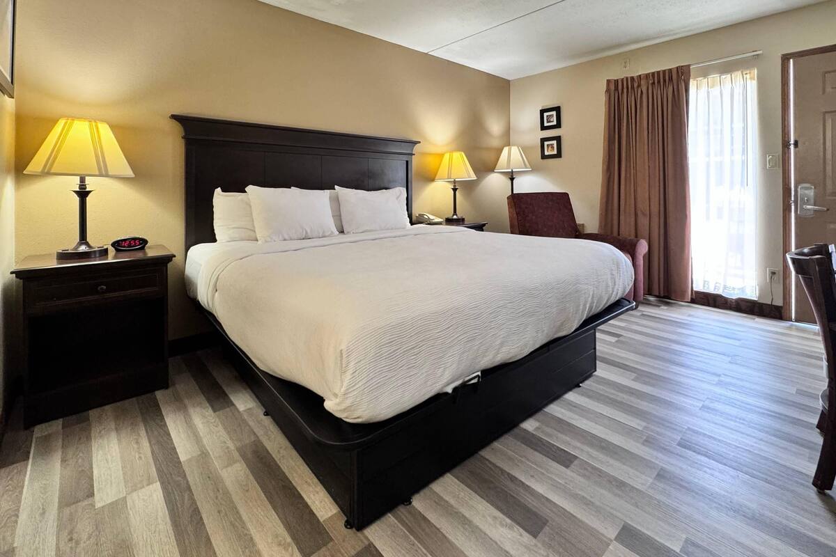 A hotel room with a large bed, two bedside tables with lamps, a chair, and a door.