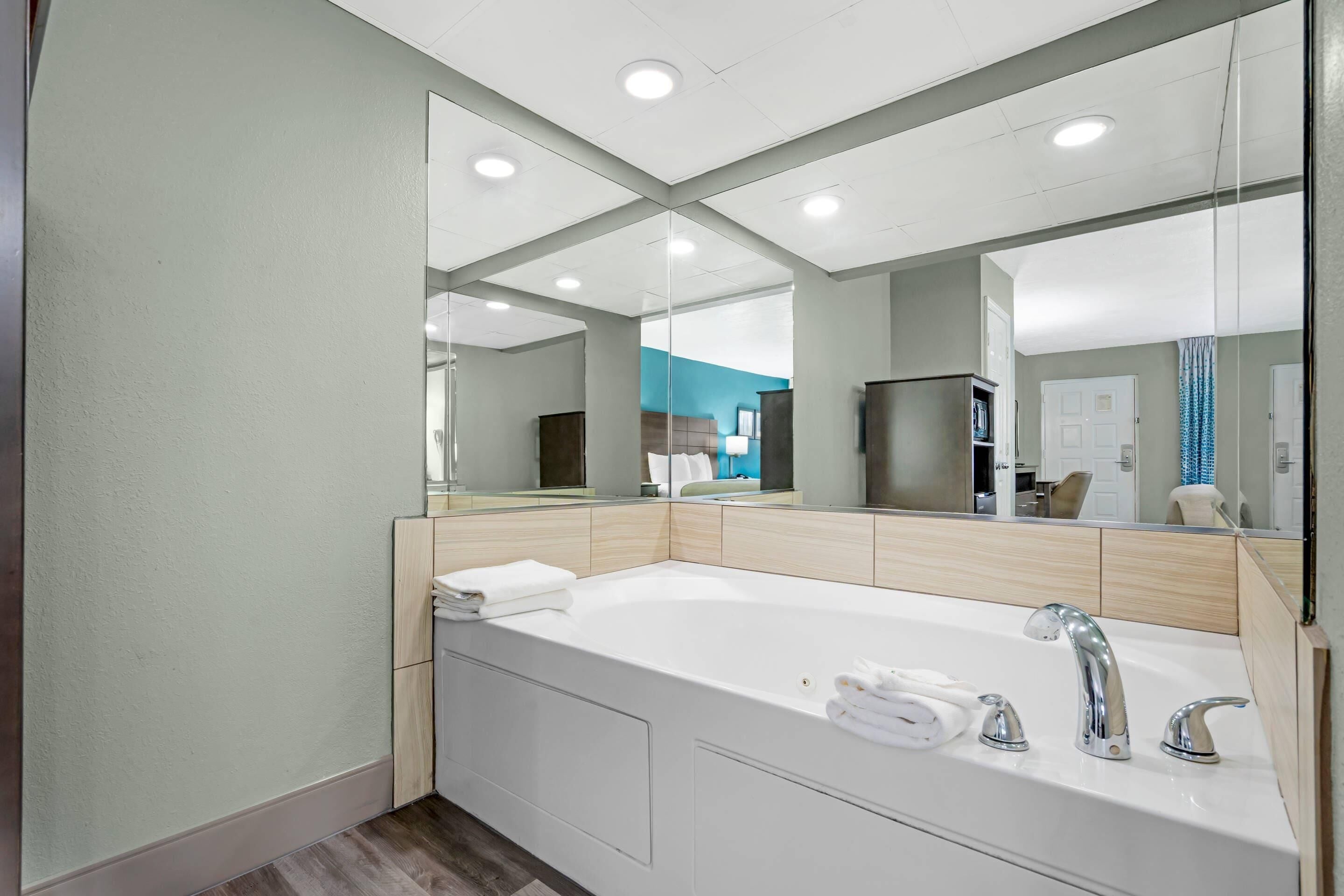 A modern bathroom with a large mirror, a white bathtub, and a sink with chrome fixtures.