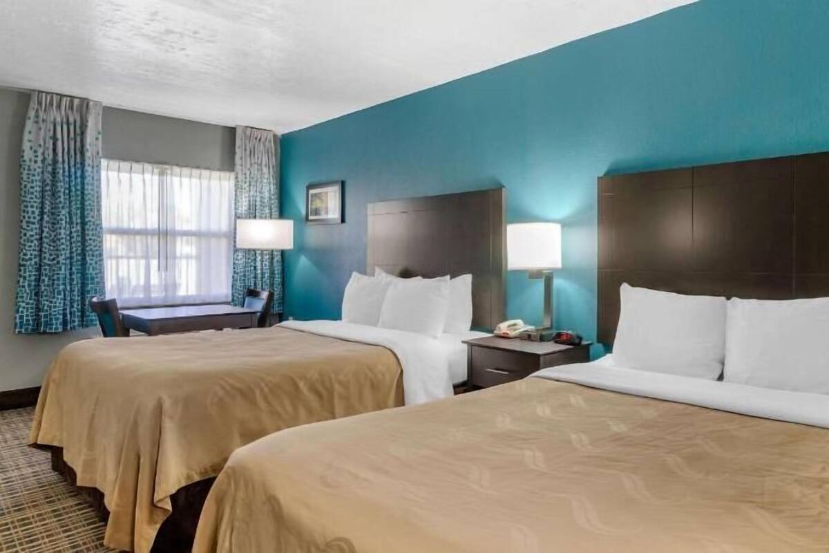 A hotel room with two beds, a desk, and a chair.