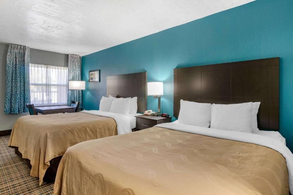 A hotel room with two beds, a desk, and a chair.