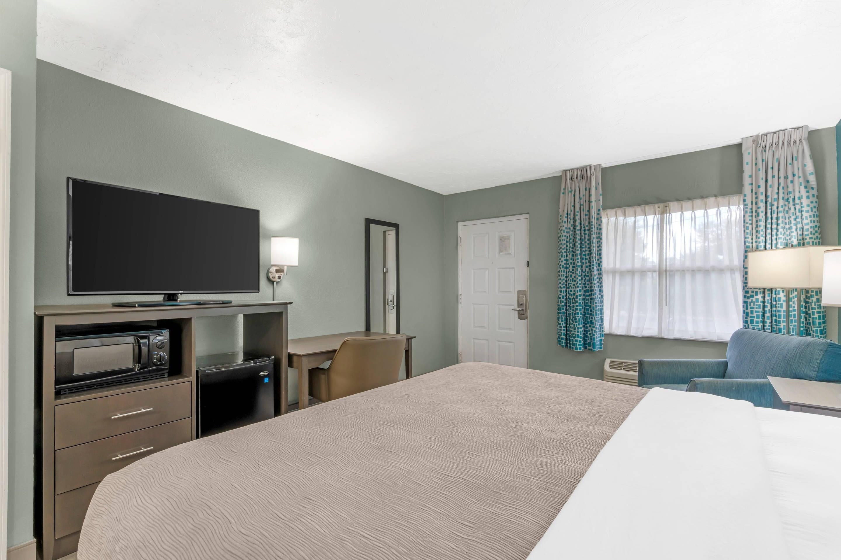Ett hotellrum med en stor säng, en platt-TV, en mikrovågsugn, ett litet kylskåp, ett skrivbord och en stol.