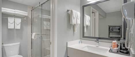 A modern bathroom with a glass-enclosed shower, a white toilet, a large mirror, and a white sink with a coffee maker.