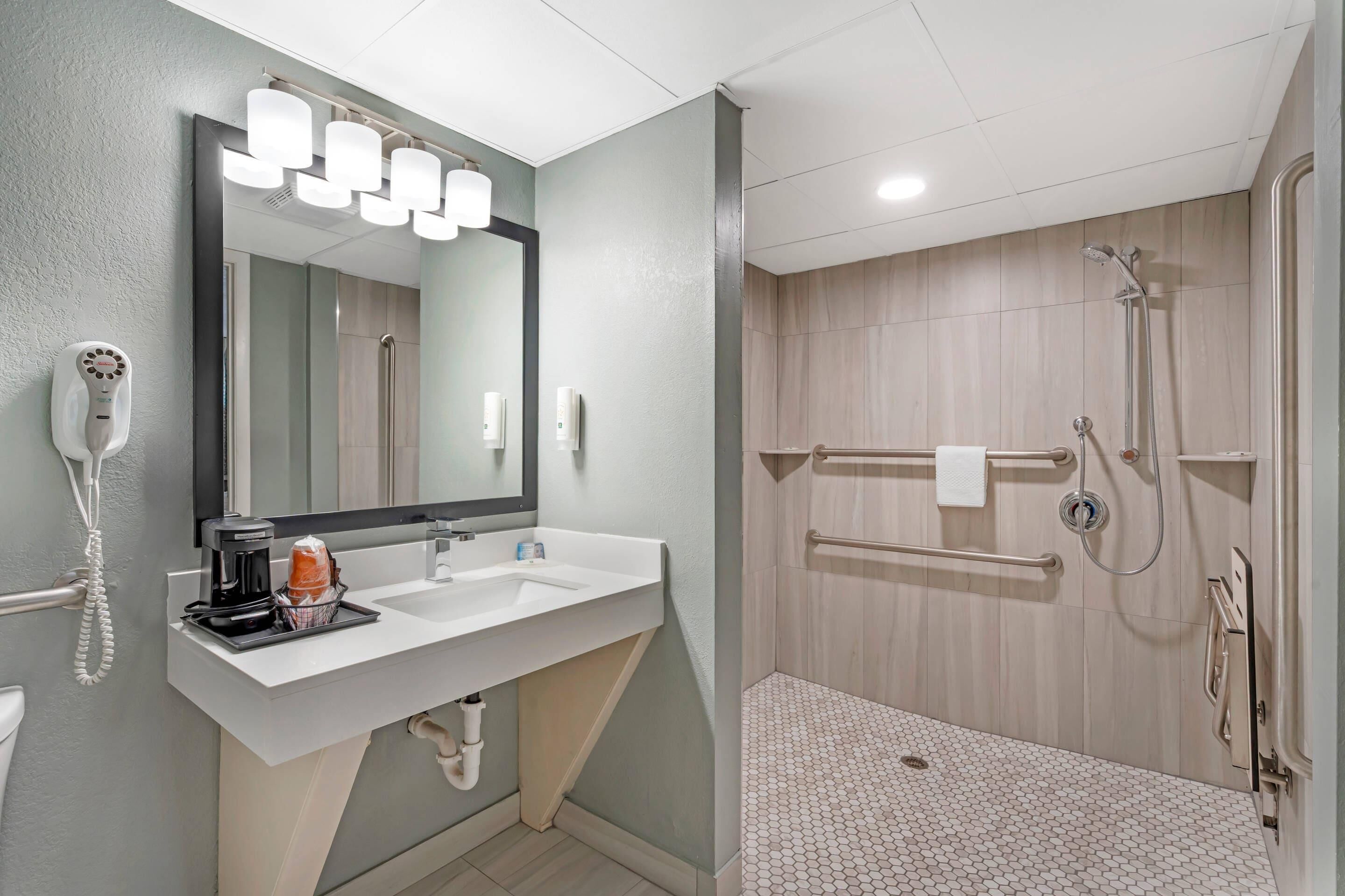 A modern bathroom with a white sink, a large mirror, and a shower area with a wooden floor.