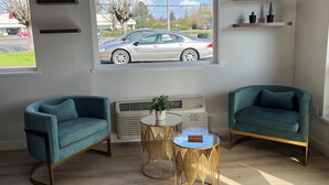 A modern living room with teal armchairs, a round gold table, and a large window with a view of a parked car and trees. - Americas Best Value Inn & Suites Forest Grove Hillsboro (Forest Grove)