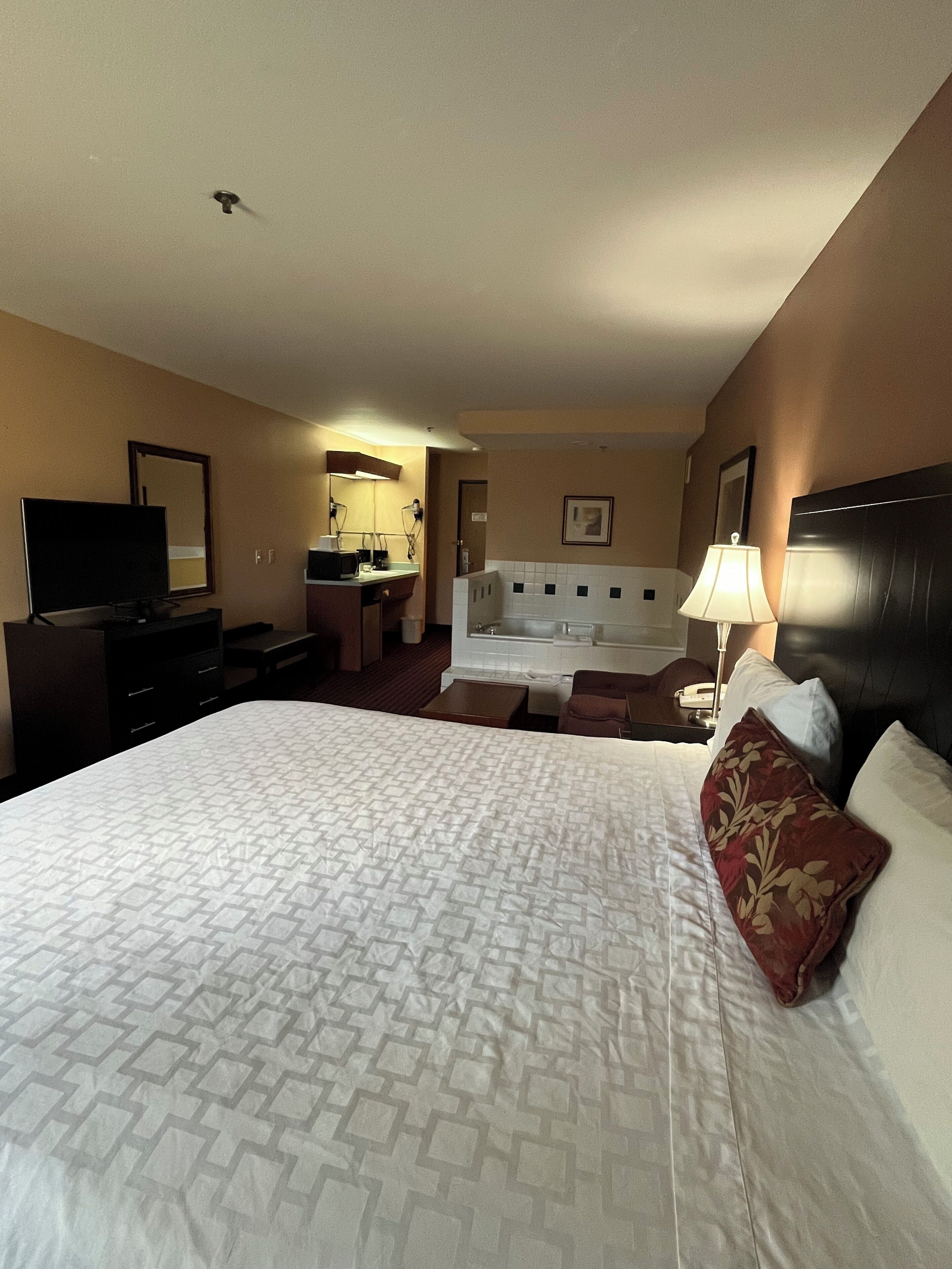 A hotel room with a large bed, a desk, a television, and a bathroom visible through an open door.