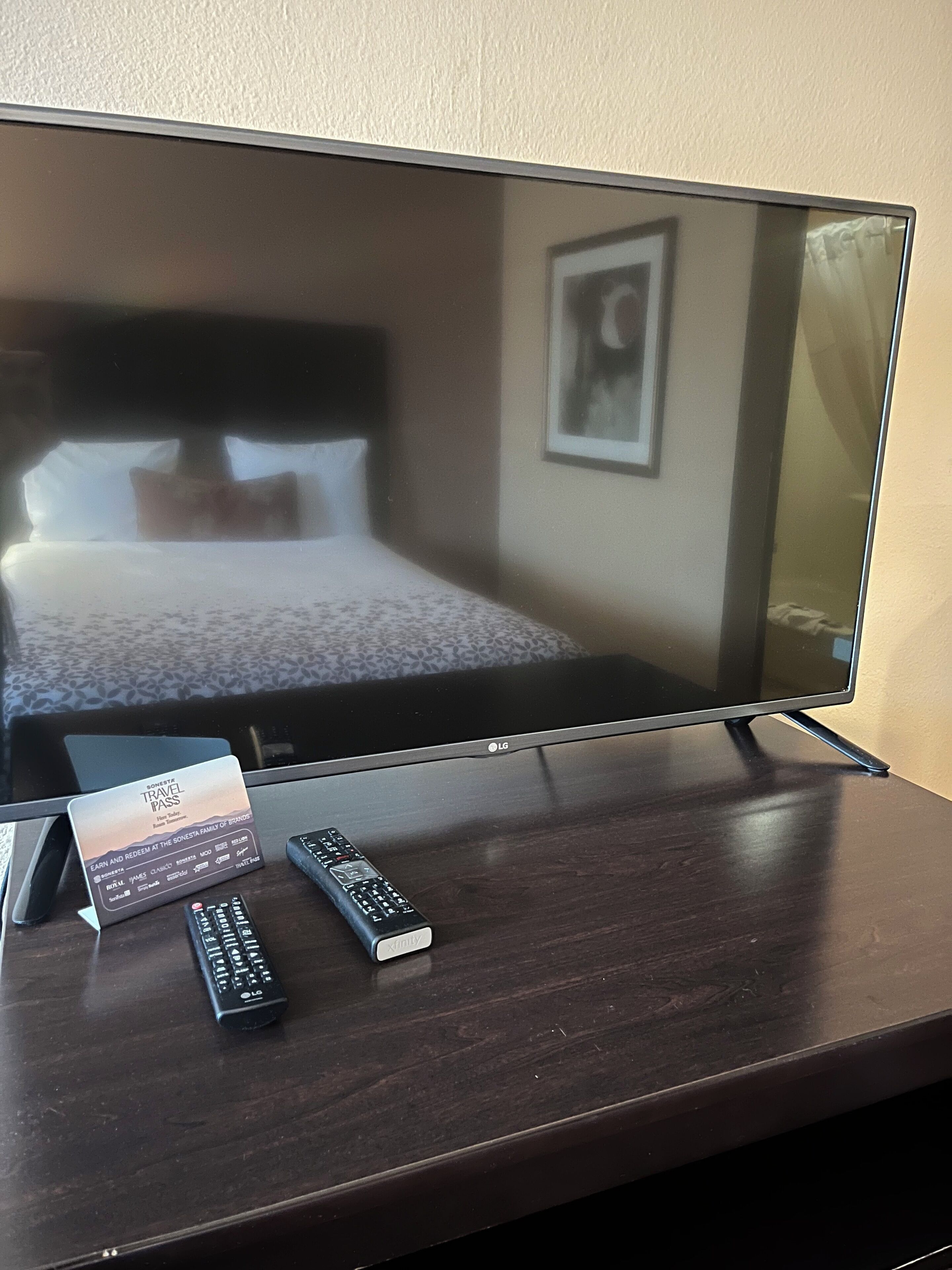 A hotel room with a television on a wooden table, two remote controls, and a travel pass card.