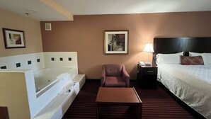 A hotel room with a bed, a chair, a table, a nightstand, a lamp, and a bathtub. - Americas Best Value Inn & Suites Forest Grove Hillsboro (Forest Grove)
