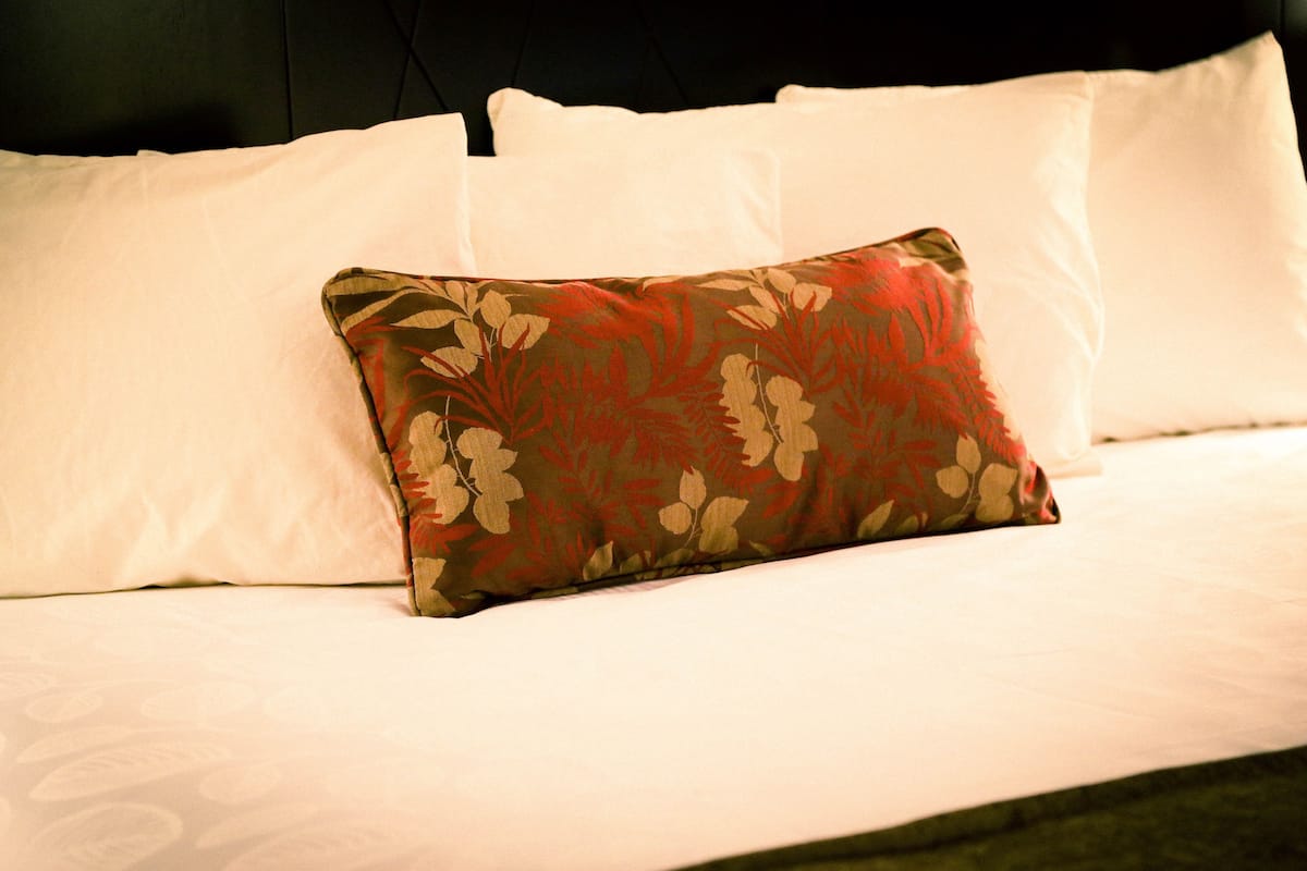 A bed with white linens and a floral-patterned pillow.