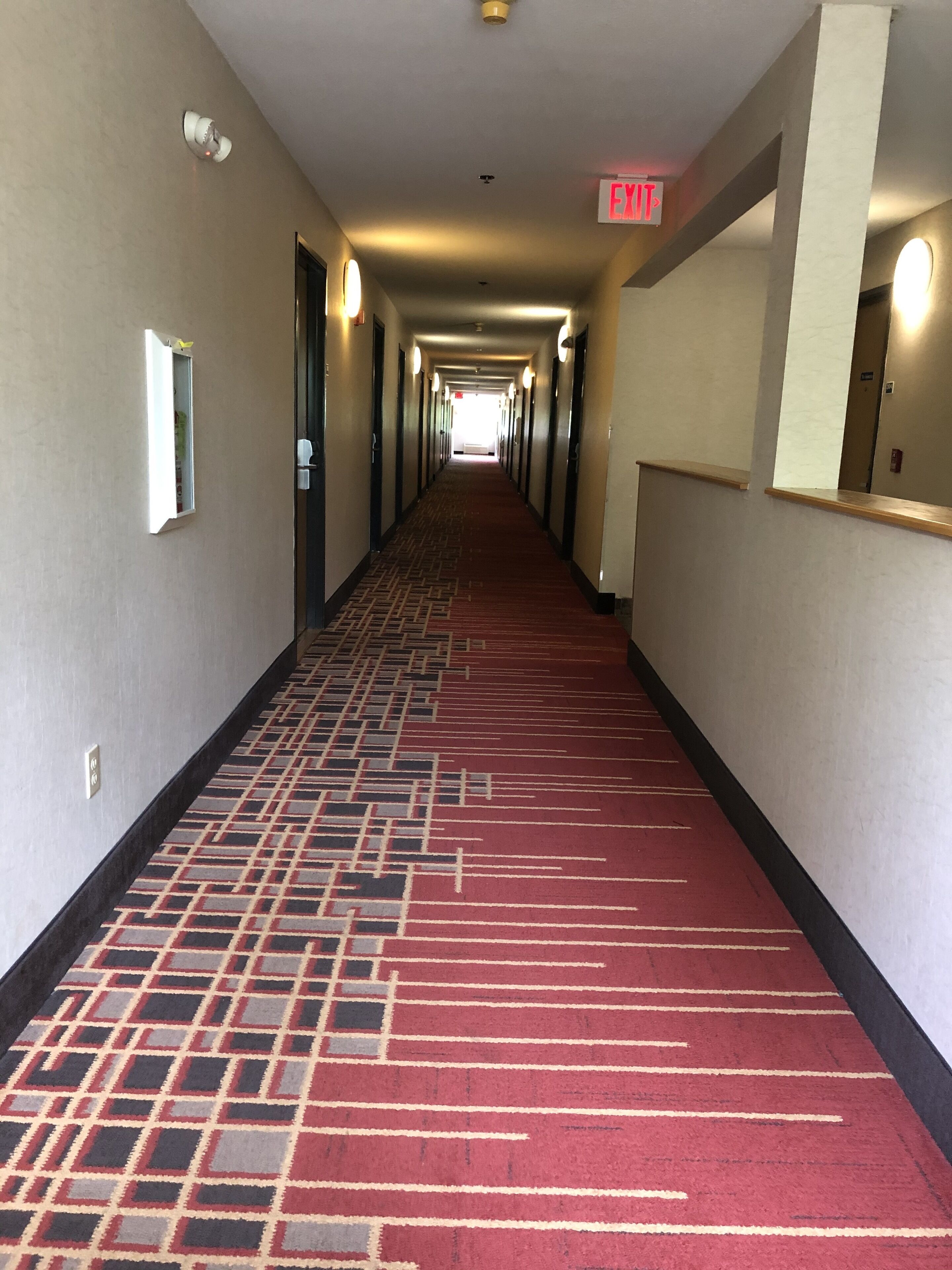 Corredor de hotel com tapete vermelho, portas em ambos os lados e sinal de saída.