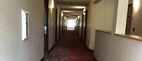 Corredor de hotel com tapete vermelho, portas em ambos os lados e sinal de saída.