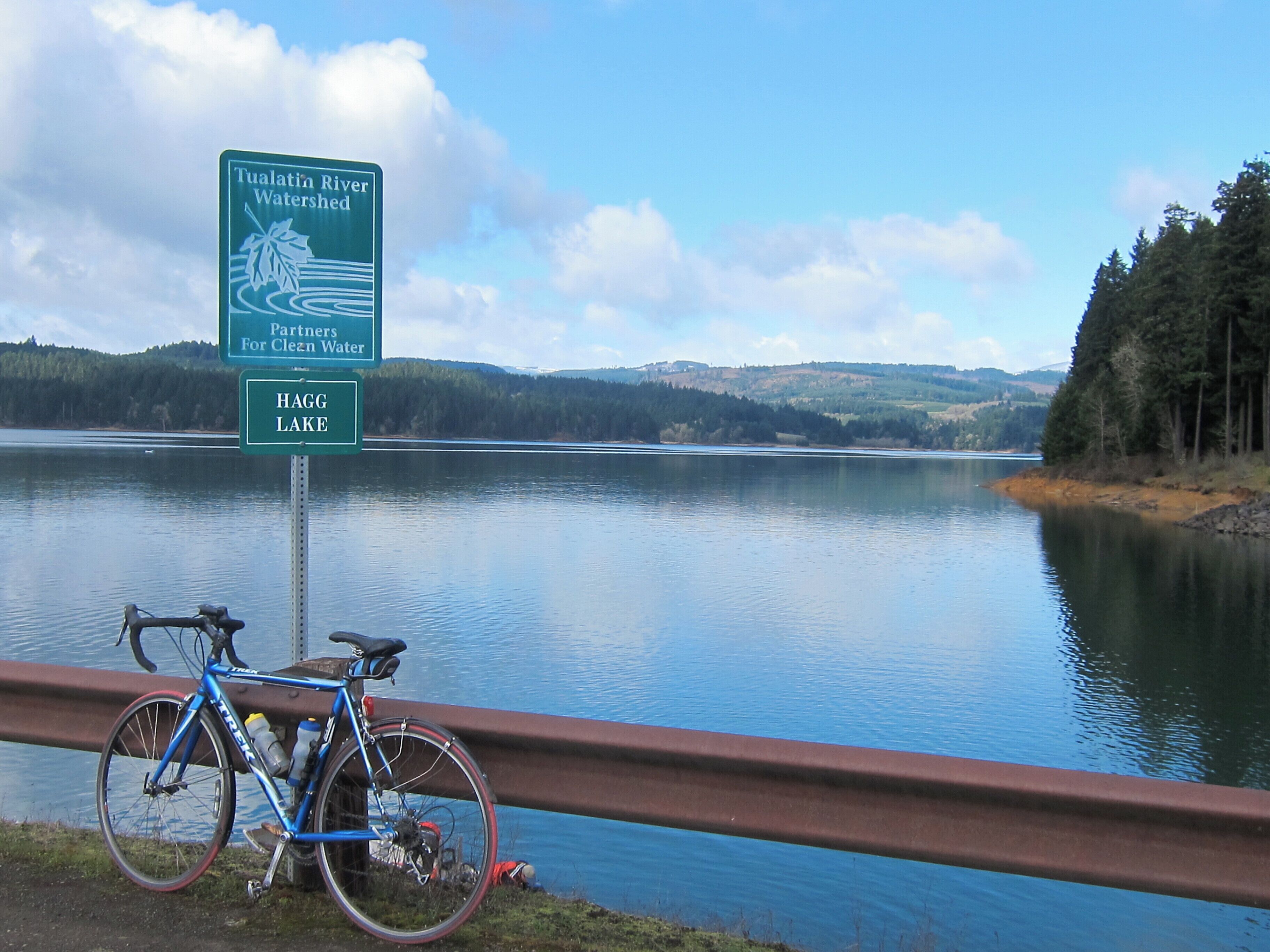 Skilt for Tualatin River Watershed og Hag Lake, med en cykel parkeret ved et gelænder med udsigt over søen.